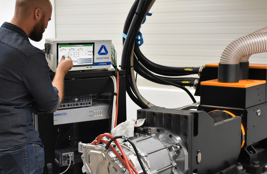 A man operates a litepa turnkey Power Analyzer control panel displaying graphs and data next to industrial machinery with cables, ducts, and exposed mechanical parts in a laboratory or workshop setting.