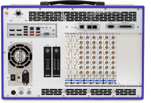 Rear view of an industrial computer or data acquisition device, showing multiple ports, slots, connectors, cooling fan, power supply inputs, and a grid of circular connectors labeled for various inputs and outputs.