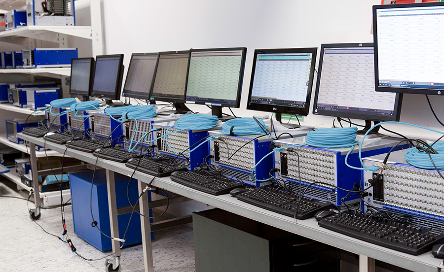 A row of computer monitors, keyboards, and blue network devices are set up on a workbench in a laboratory or technical workspace, with cables—and possibly pydmdreader python scripts—connecting each device.